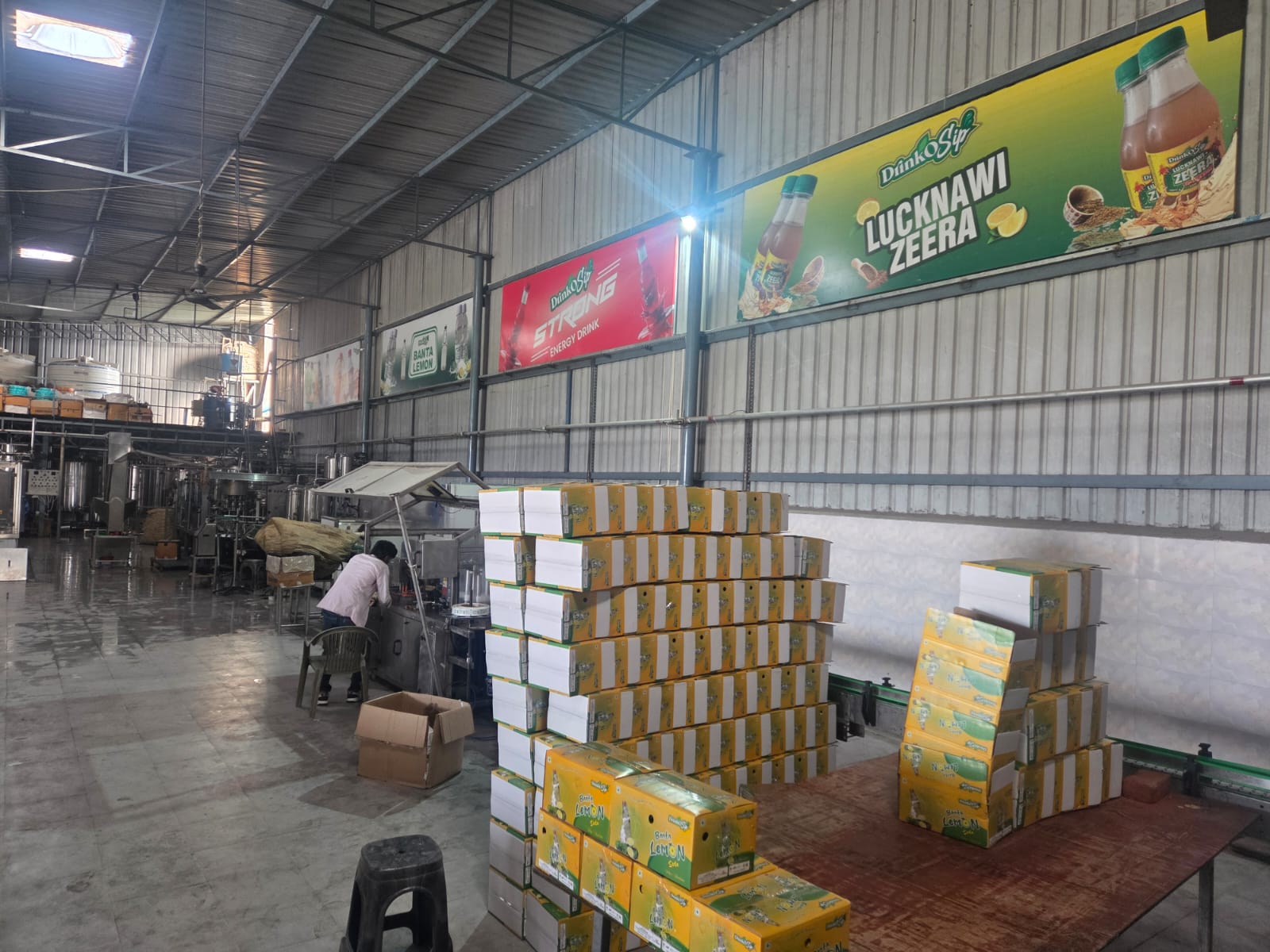 Production floor with finished cases under DrinkoSip brand banners